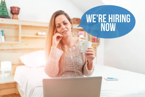 Firma mostrando We Re Hiring Now. Concepto de Internet recientemente emplear a alguien o pagar a alguien para hacer un trabajo en particular Mujer vediocalling a través de la computadora portátil desde el dormitorio con auriculares con cable — Foto de Stock