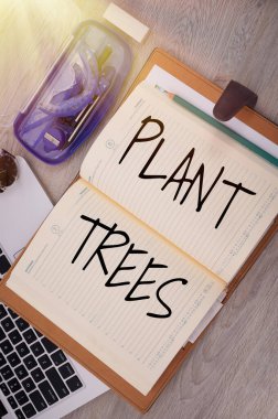 Metin işareti Bitki Ağaçlarını gösteriyor. Arazi ekimi ve ormancılık için ağaç dikme süreci Pusula Kalem Saati olan bir dizüstü bilgisayarın üzerine Boş Not Defteri