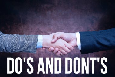 Kavramsal başlık Do S and Don 't S. İş Gösterisi Kuralları ya da bazı faaliyetler ya da eylemlerle ilgili iki profesyonel iyi giyimli iş adamı kapalı mekanda el sıkışıyor.
