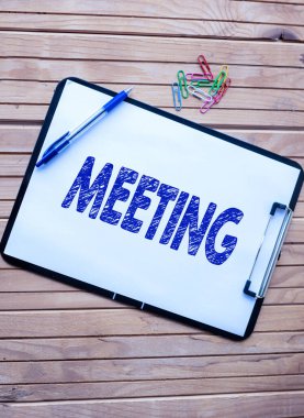 Toplantıyı sunan metin başlığı. Özel bir amaç için ya da resmi tartışma için toplanan sözcük Sade Ofis Panosu ile Bir Holder 'daki Kalem Yığını Masaya Yerleştirilmiş.