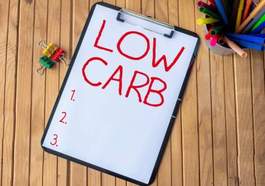 El yazısı düşük karbonhidrat. İş yaklaşımı, karbonhidrat tüketimi tüketimi azaltma diyetini kısıtlıyor. Masanın üstüne konmuş kalem yığınları ile ofis panosu..