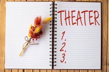Tiyatroyu gösteren tabela. Konsept, oyunun oynandığı ve dramatik performansların yapıldığı bina veya açık alan anlamına gelir. Üzerinde renkli bir çiçek olan ve ahşap bir masaya yerleştirilmiş bir defter açın.