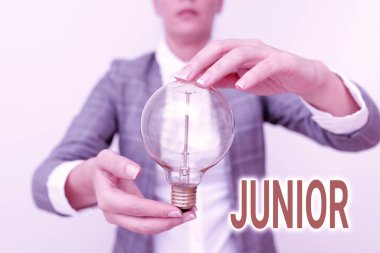 El yazısı tabelası Junior. Başka birinden kaç yaş küçük olduğu belirtilmiş bir iş adamı olan Erson. Kıyafet lambası taşıyan kadın, iki eliyle yeni teknoloji fikirleri sunuyor.