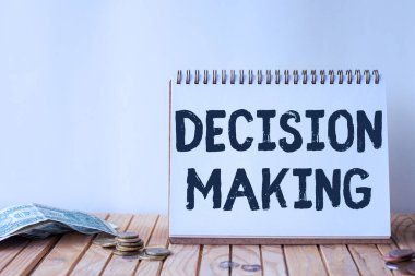 Metin Kararı Yazma Yazılıyor. İki veya daha fazla olasılık arasında karar verme eylemi üzerine yazılmış sözcük. Boş Spiral Not Defteri Masanın Üzerinde Para Yığını.