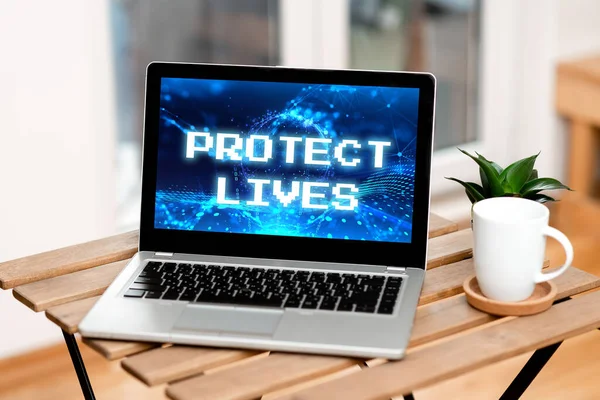 Text caption presenting Protect Lives. Business overview to cover or shield from exposure injury damage or destruction Laptop Resting On A Table Beside Coffee Mug And Plant Showing Work Process.