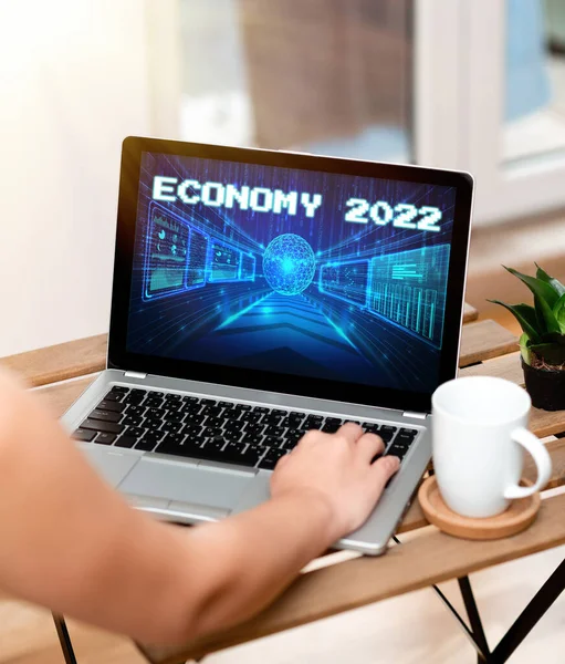 Handwriting text Economy 2022. Business showcase State of wealth and resources of a country in upcoming year Hand Busy Typing On Laptop Beside Coffe Mug And Plant Working From Home. — Foto Stock