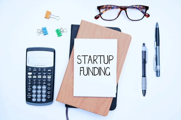 Text sign showing Startup Funding. Word for financial investment in the development of a new company Office Supplies Over Desk With Keyboard And Glasses And Coffee Cup For Working — Stock Photo, Image