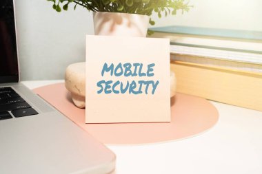 Metin Mobil Güvenlik yazılıyor. İş genel değerlendirmesi cep telefonunun tehditlerden ve savunmasızlıklardan korunması ofis malzemeleri klavye, bardak ve çalışma için kahve fincanı.