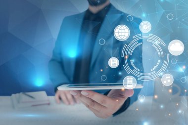 Takım elbiseli bir işadamı elinde tablet ile başarılı bir takım çalışmasının sembolü olarak yeni proje planlarını gerçekleştiriyor. Elektrikli cihaz taşıyan adam birleşik çaba yönetimini temsil ediyor.