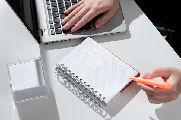 Woman Writing In Notebook With Marker On Desk With Notes And Lap Top.