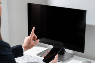 İş kadını cep telefonunu tutuyor ve bilgisayar ekranını işaret ediyor..