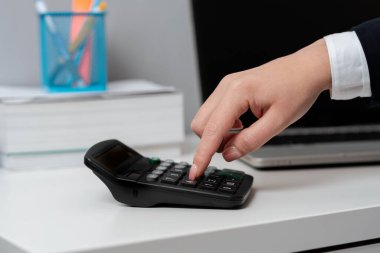 Hesap makinesine basan bir kadın, bir parmağı masanın üstünde, üstü ve kitapları var.