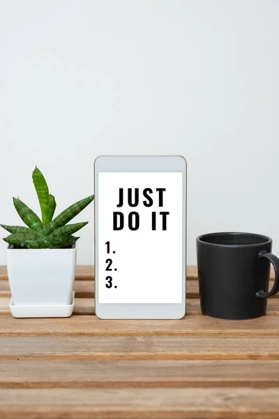 Hand writing sign Just Do It, Business concept Motivation for starting doing something Have discipline Tablet With Important Information On Table With Plant And Cup Of Coffee.