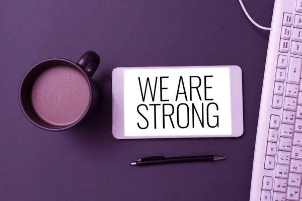 Conceptual display We Are Strong, Concept meaning Have great strength healthy powerful achieving everything Phone Screen With Important Message On Desk With Keyboard, Pen And Coffee.