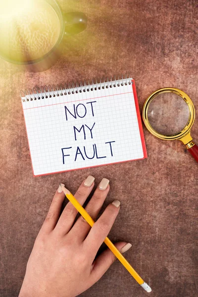 Text sign showing Not My Fault, Word Written on To make excuses to avoid being accused for a mistake error Hand Of Woman Spiral Notebook, Magnifying Glass And Coffee Cup On Wood.