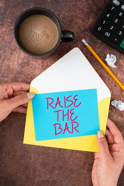 Sign displaying Raise The Bar, Business showcase Set higher standards challenges seeking for excellence Woman Holding Blank Letter With Coffee And Stationery Over Wood.
