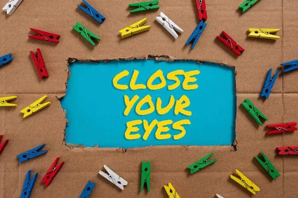 Hand writing sign Close Your Eyes, Business concept Cover your sight we have a surprise for you do not peek Important Ideas Written Under Ripped Cardboard With Colored Pegs Around.