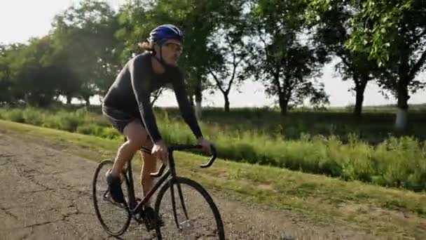 Jovem ciclista em passeios de capacete de bicicleta ao longo da estrada aspalt, vista lateral — Vídeo de Stock