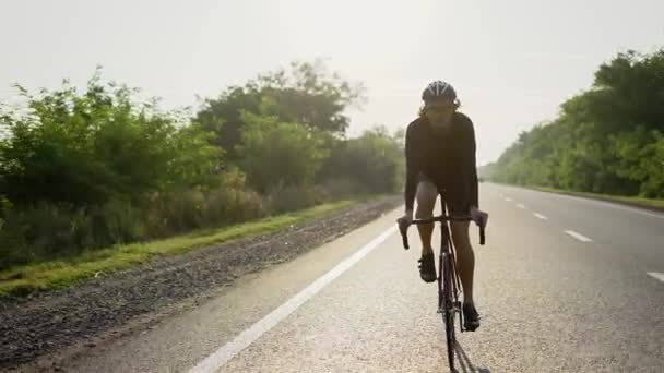 Ciclista maschio in casco cavalca bicicletta lungo una pista vuota, vista frontale — Video Stock