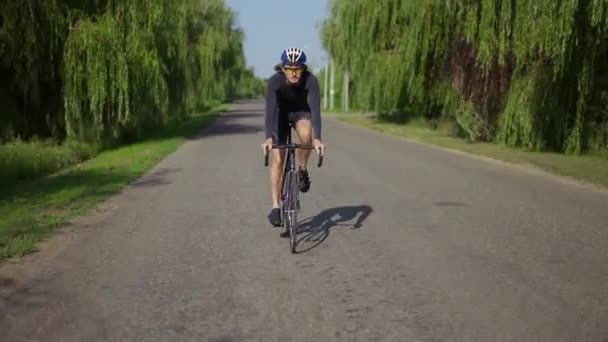 Чоловічий велосипедист в шоломі їде на велосипеді вздовж колії, набираючи швидкість, вид спереду — стокове відео
