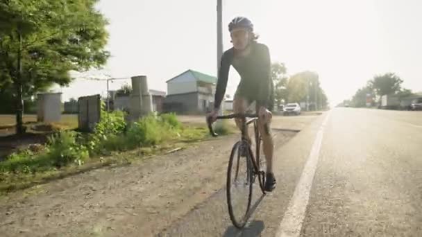 Um ciclista profissional do sexo masculino anda de bicicleta ao longo da estrada lateral do país — Vídeo de Stock