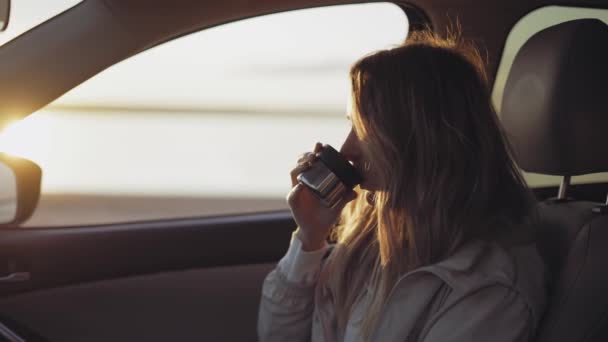 Femme à l'intérieur de la voiture boit du café dans la tasse thermos, adorant lever de soleil — Video