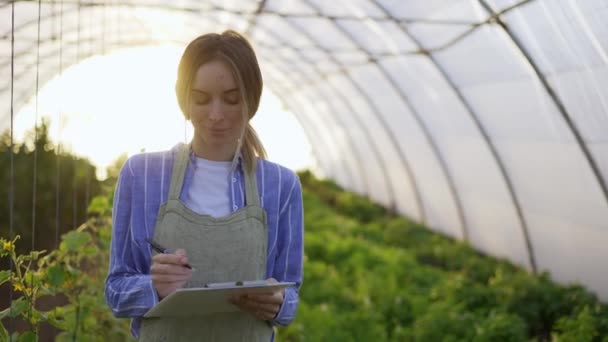 Ung kvinna bonde i inomhus växthus, bokföring växter med hjälp av tablett — Stockvideo