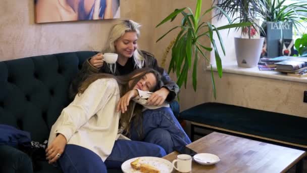 Glückliches lesbisches lgbtq verliebtes Paar kuschelt, lacht, trinkt Kaffee, hat Spaß auf der Couch im Café — Stockvideo