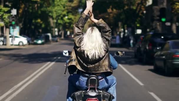 Blond kvinna passagerare njuter av ridning motorcykel vid staden, bakre vy — Stockvideo