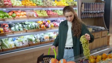 Kadın müşteri yemek reyonundan üzüm alıyor.