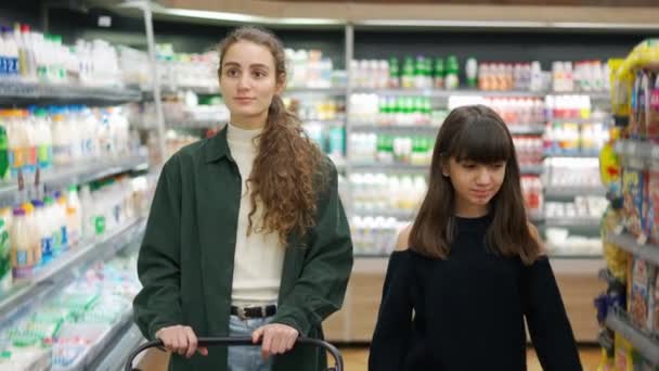 Adolescente chica y su mamá o hermana de compras en el supermercado con carro — Vídeo de stock