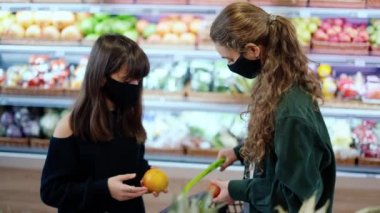Maskeli iki kadın süpermarkette biyolojik meyveleri birlikte seçiyor.