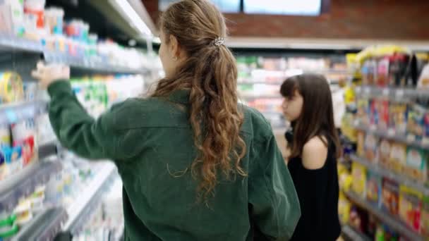 Adolescente chica y su mamá o hermana de compras en el supermercado con carro, vista trasera — Vídeo de stock