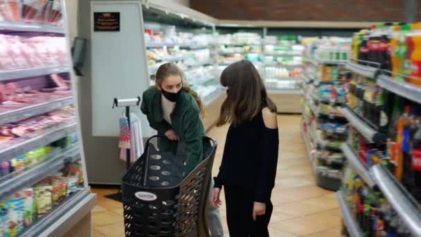 Adolescente et sa mère ou sa sœur faisant du shopping au supermarché avec chariot, portant des masques — Video