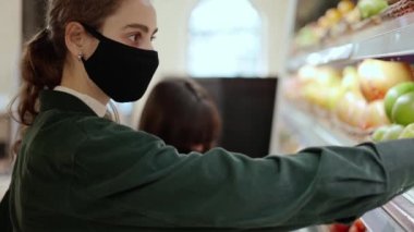 İki kadın süpermarkette biyolojik meyveleri birlikte seçiyor, maske takıyor.