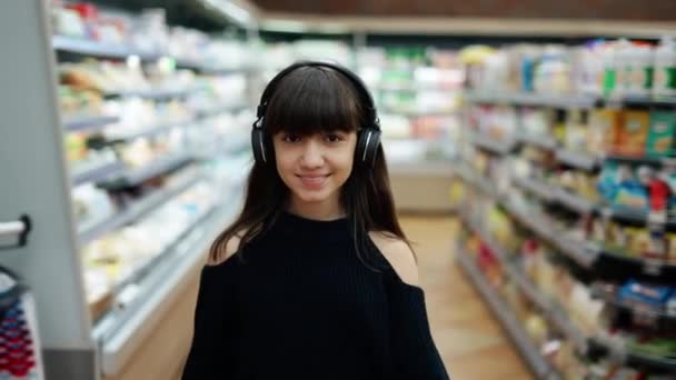 Sonriente adolescente caminando en el supermercado en auriculares — Vídeos de Stock
