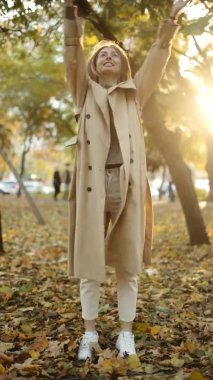 Sonbaharda yaprakları yavaş çekimde atan mutlu bir kadın. Gülümsüyor, uzun boylu.