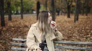 Kahve içen kadın sonbahar parkında çikolata yiyor.