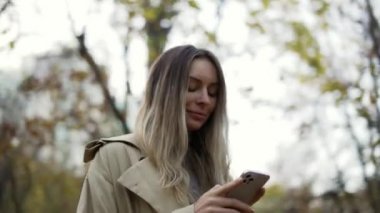 Sonbahar parkındaki telefondan mesaj okuyan ya da internette sörf yapan bir kadın.