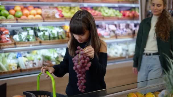 Hermosas chicas eligiendo frutas bio uva en el supermercado juntos — Vídeos de Stock