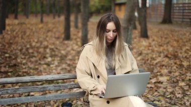 Avrupalı görünümlü genç bir kadın bir dizüstü bilgisayarda çalışıyor, bir bankta oturuyor.