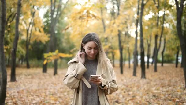 Tânăra femeie de frumusețe scrie un mesaj pe telefonul mobil într-un parc de toamnă — Videoclip de stoc