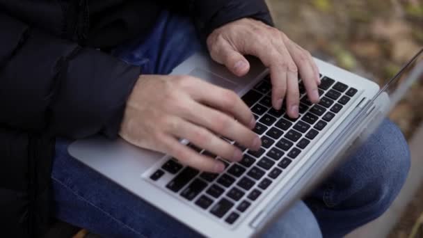 Onherkenbare man zittend op de bank in het park, typend op de laptop — Stockvideo