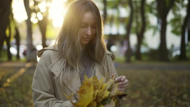 Cheerful woman with pile of golden leaves in hands in sunny autumn park — Stock Video