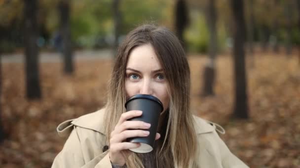 Portrait of a blonde woman drinking take away coffee in the golden, autumn park — Stock Video