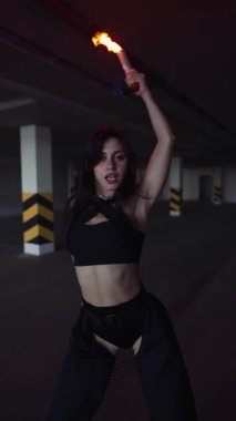Seksi kadın modern dans gösterisi yapıyor, park yerinde kameraya poz veriyor. Karanlık ışıkta, alev makinesiyle.