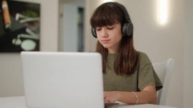 Kulaklıklı, dizüstü bilgisayarın önünde oturan sevimli genç kızın portresi.