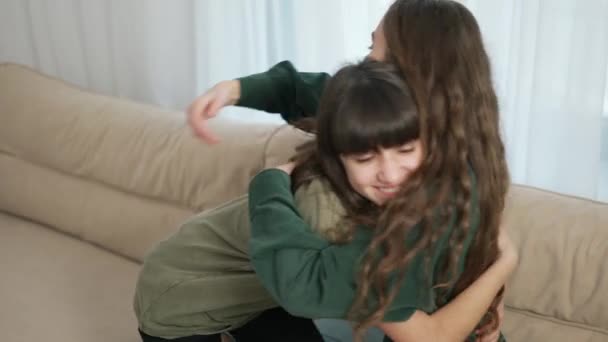 Близкие отношения. Ласковые молодые мама и дочь обнимаются на диване дома — стоковое видео