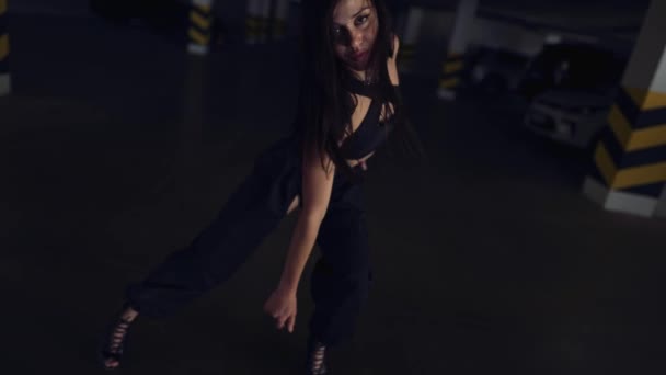 Κομψή γυναίκα εκτελεί μοντέρνο χορό, ποζάροντας στην κάμερα σε ζώνη στάθμευσης σε σκούρο φως — Αρχείο Βίντεο