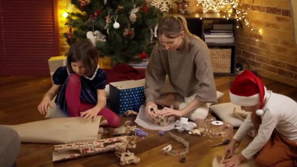 Mère et enfants enveloppant des cadeaux de Noël ensemble sur le sol — Video